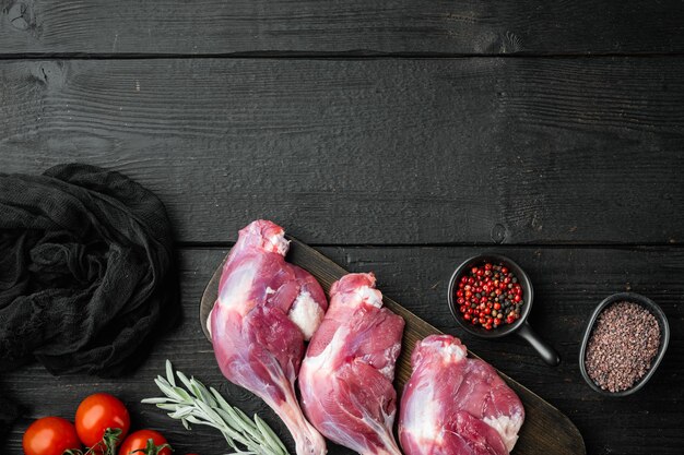 Pernas de pato cru. Conjunto de carne de frango pronta para cozinhar, com ervas e ingredientes, em mesa de madeira preta