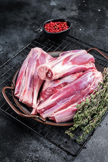 Pernas de perna de cordeiro cru em uma bandeja de aço com ervas Fundo preto Vista superior