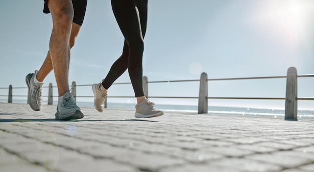 Pernas de pessoas e correndo na praia para exercícios aeróbicos ou treinando juntos ao ar livre Perna de amigos caminhando ou correndo em um dia quente e ensolarado na costa do oceano para um bem-estar saudável