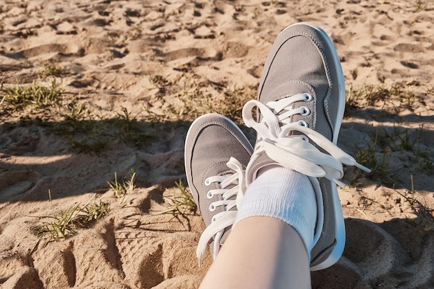 Pernas de tênis cinza na areia da praia conceito de férias de verão à beira-mar viagem de estilo de vida