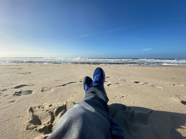Pernas de terapia do mar de um menino que está relaxando na praia olhando as ondas do mar e o céu azul