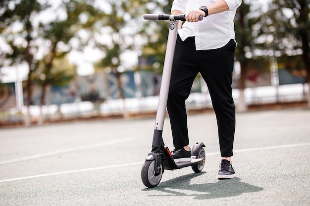 Pernas de um homem em uma roupa elegante ficam em scooter elétrico na rua.