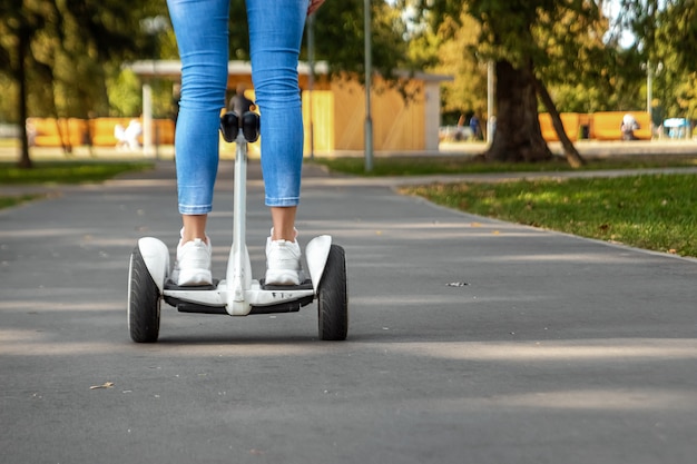 Pernas de uma garota de tênis branco em um hoverboard branco em um close-up do parque