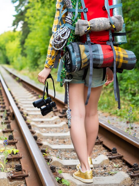 Pernas de uma mulher com uma mochila caminham ao longo da ferrovia com binóculos. vista traseira.