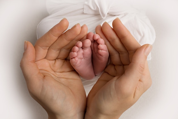 Pernas, dedos, pés e calcanhares de um recém-nascido. Com as mãos dos pais, pai, mãe e irmã, o irmão segura delicadamente as pernas da criança. Foto em preto e branco. Foto de alta qualidade