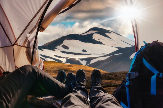 Pernas do casal viajante relaxando dentro de uma tenda com montanha vulcânica na área geotérmica nas terras altas da islândia no verão