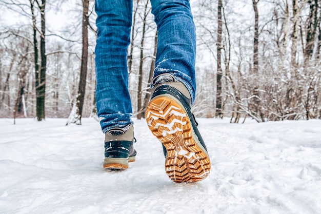 Pernas do homem em botas andando na neve