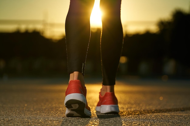 Pernas e pés femininos andando de tênis no asfalto sob o sol do sol