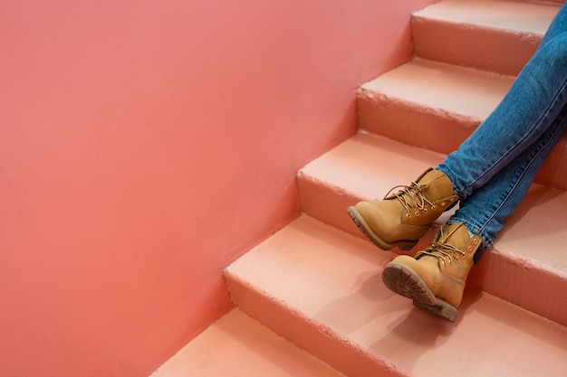 Pernas em botas marrons de jeans azul na escada rosa copiam o espaço para publicidade relaxam o conceito de cor