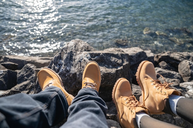 Pernas em jeans e botas nas rochas perto do lago de montanha com reflexo de água