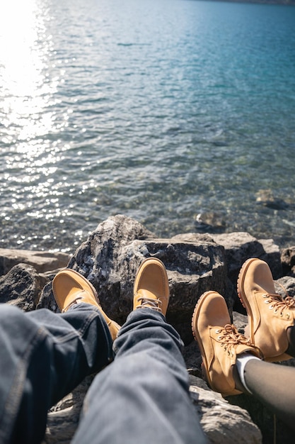 Pernas em jeans e botas nas rochas perto do lago de montanha com reflexo de água