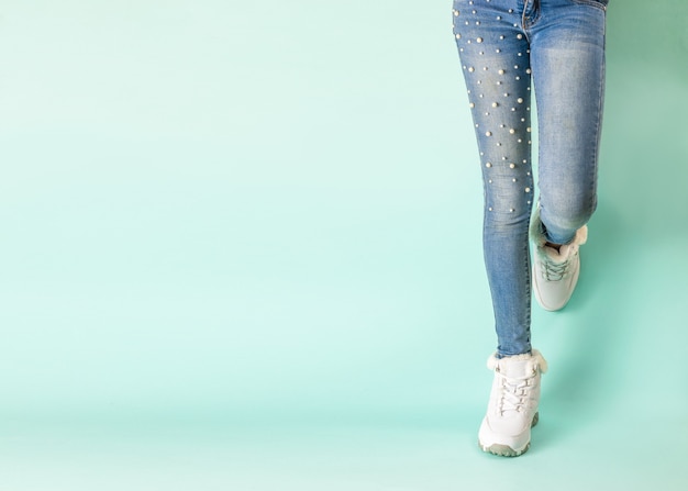 Pernas em jeans justos e tênis branco de inverno contra a parede azul