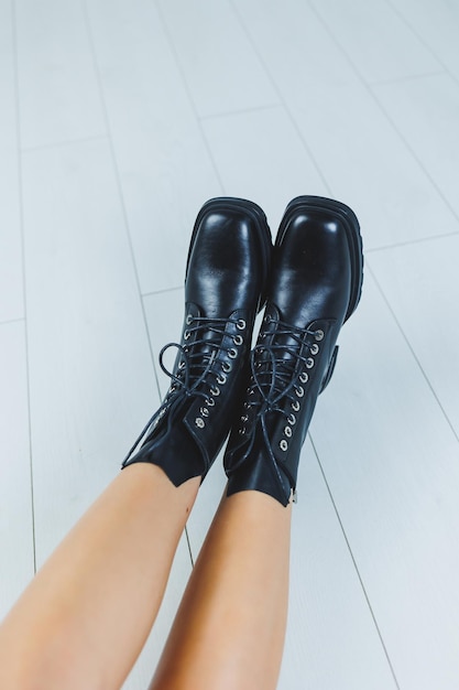 Pernas femininas em botas de outono pretas de couro Uma garota fashion fica em uma loja e mede sapatos