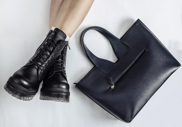 Pernas femininas em botas pretas de couro na moda e bolsas em um fundo branco