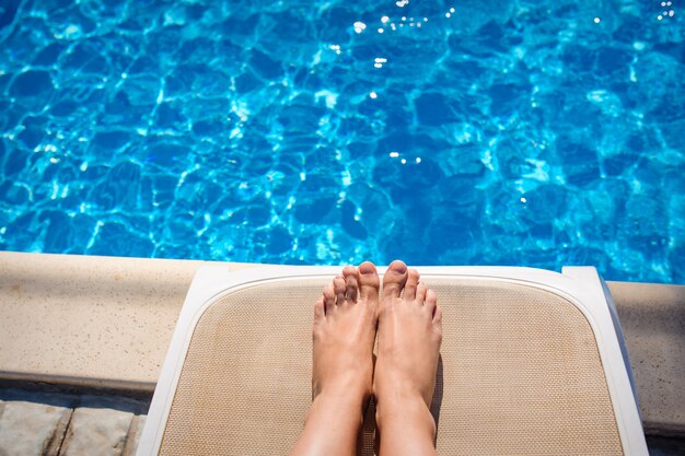 Pernas femininas em uma espreguiçadeira no fundo da piscina