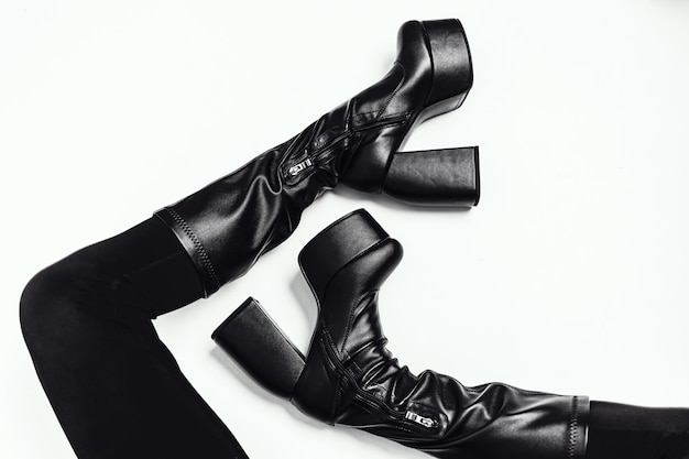 Pernas femininas esbeltas em botas de couro preto sobre fundo branco Sapatos da moda na plataforma alta