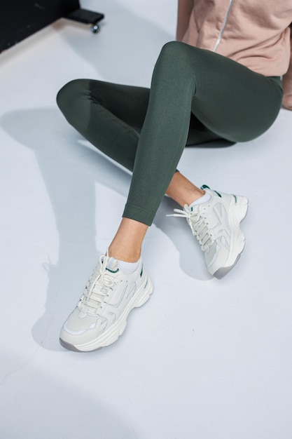 Pernas femininas finas em leggings e tênis casuais elegantes brancos Sapatos de verão confortáveis para mulheres