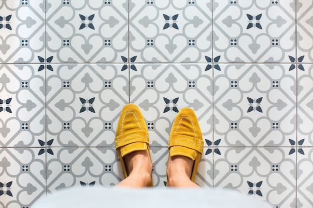 Pernas femininas, pés em sapatos amarelos em um piso de ladrilho de mosaico. vista de cima, selfie plana em um fundo vintage sem costura, copie o espaço