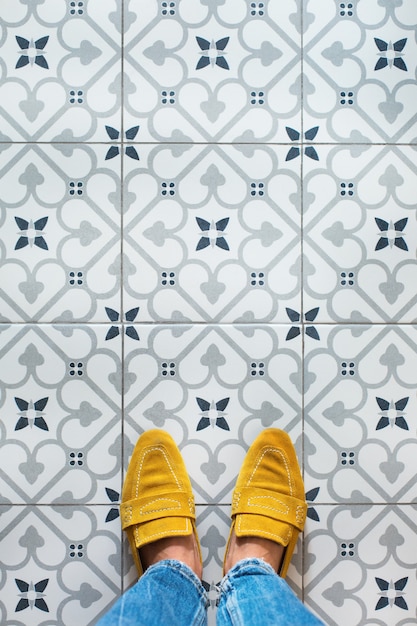 Pernas femininas, pés em sapatos amarelos em um piso de ladrilho de mosaico. vista de cima, selfie plana em um fundo vintage sem costura, copie o espaço