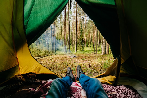 Pernas masculinas deitado na barraca de acampamento com vista para a floresta