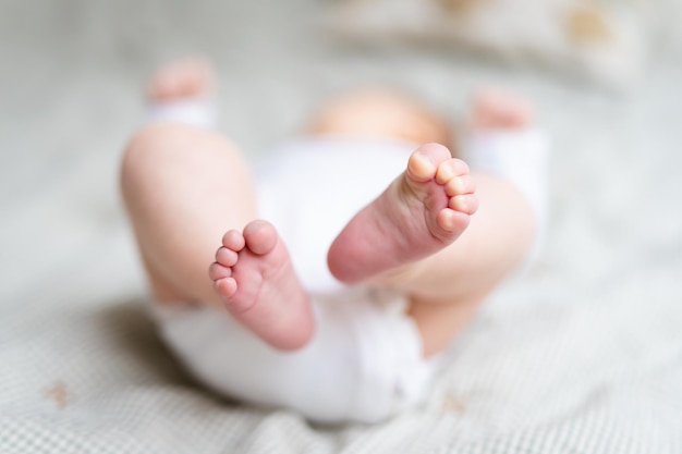 Pernas minúsculas de bebê fecham recém-nascido vestindo corpo deitado na cama primeiros dias em casa após o nascimento conceito de cuidados com o bebê