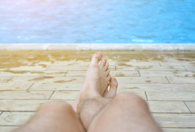 Pernas peludas de um homem contra um fundo de água azul pura em uma piscina