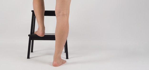Pernas traseiras e pés descalços em um banquinho de madeira ou escada em um fundo branco.