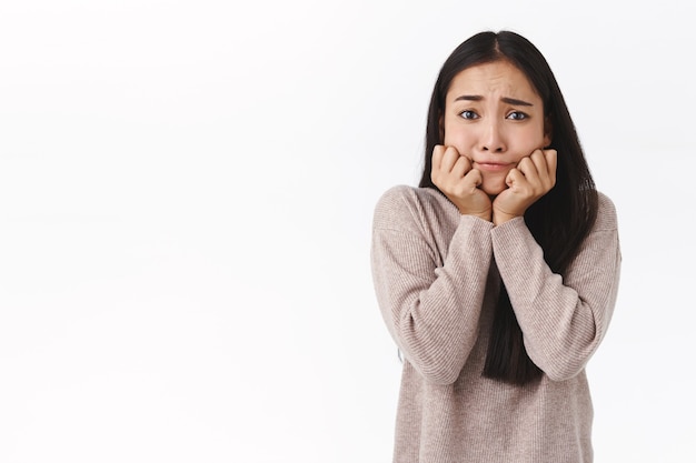 Perpleja, preocupada tonta linda adorable niña asiática con cabello largo oscuro, tomarse de las manos en la línea de la mandíbula, mirar indeciso y triste, tener problemas, enfrentar una decisión problemática, estar preocupada y molesta