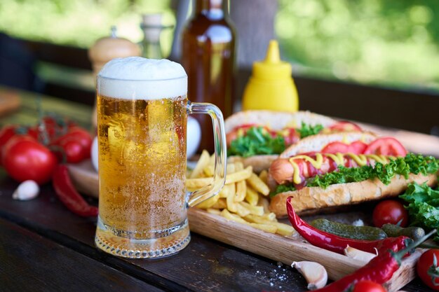 Perrito caliente a la barbacoa servido con verduras y papas fritas y salsas en una tabla de servir de madera