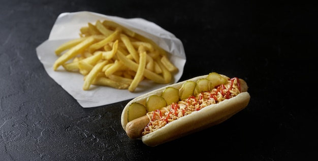 Perrito caliente con papas fritas sobre un fondo negro. Concepto de comida rápida