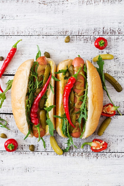 Perrito caliente con pepinillos, alcaparras y rúcula en mesa de madera.