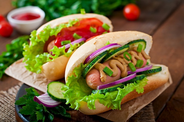 Perrito caliente con salsa de tomate, mostaza, lechuga y verduras en la mesa de madera