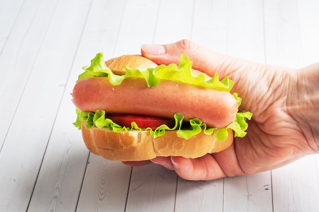 Perrito caliente con tomate lechuga y salchichas en manos.