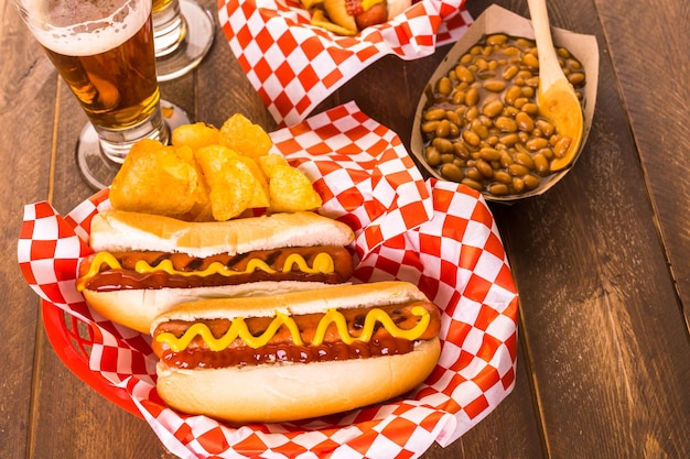 Perritos calientes a la parrilla con mostaza y salsa de tomate en la mesa con cerveza de barril.