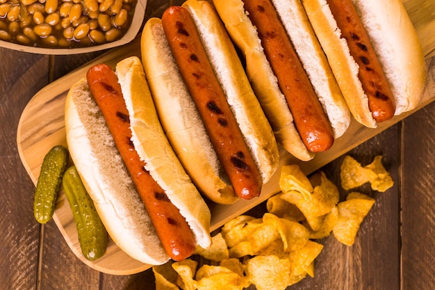 Perritos calientes a la parrilla en un pan de hot dog blanco con patatas fritas y frijoles al lado.