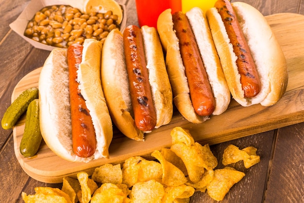 Foto perritos calientes a la parrilla en un pan de hot dog blanco con patatas fritas y frijoles al lado.