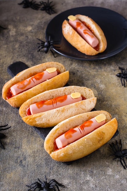 Perritos calientes de salchicha y queso en ketchup en bollos en pizarra Receta de Halloween Vista vertical