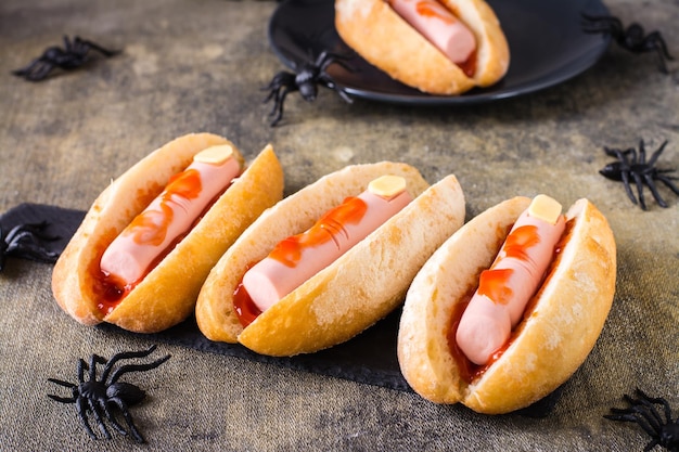 Perritos calientes de salchicha y queso en ketchup en bollos en pizarra Receta de Halloween