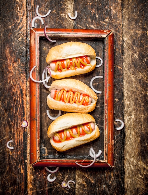 Perritos calientes con salsa de tomate y mostaza en mesa de madera.