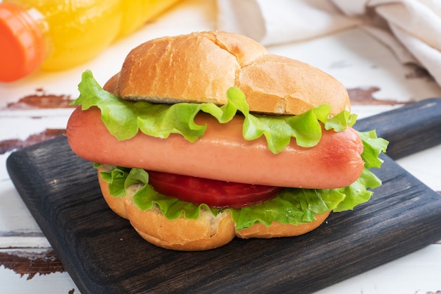 Perritos calientes en una tabla de madera. Hot dog con lechuga tomate y salchicha. Copia espacio