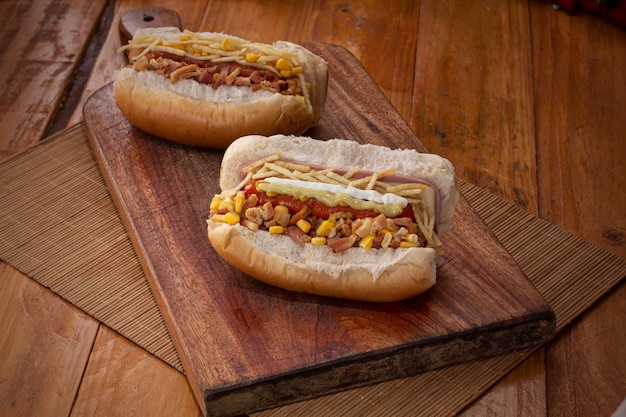 Perritos calientes en una tabla de madera rodeados de especias y verduras como tomates, pimientos y cebollas.