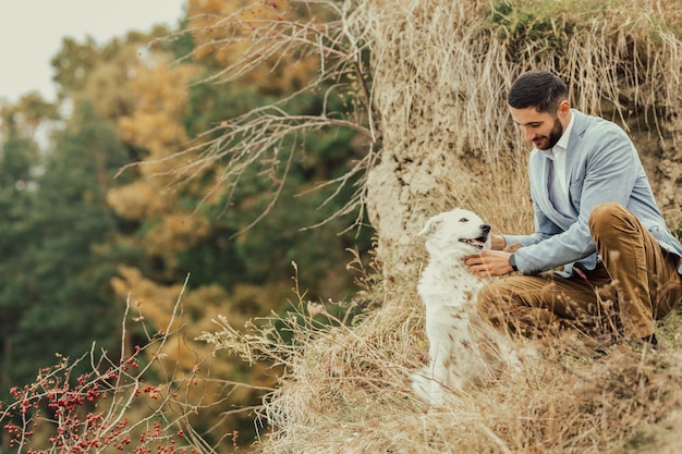 Perro blanco y joven sonriendo en el bosque