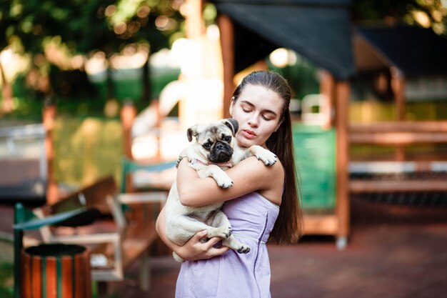 Perro feliz y niña La niña está jugando con un perro Mujer joven caminando con un perro pug en el parque de verano Retrato de un pug Retrato de un hermoso cachorro pug El perro está tirado en el suelo