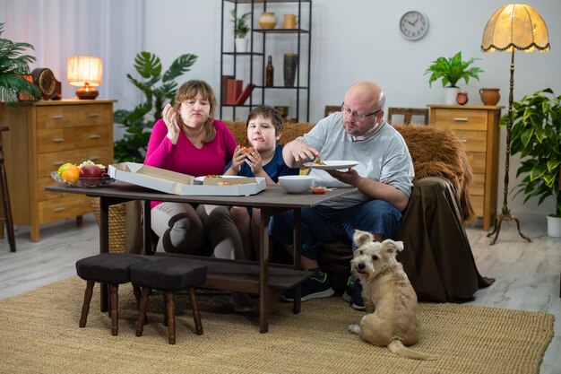 Un perro impaciente mira a su alrededor por una segunda pizza. La familia consume la pizza.