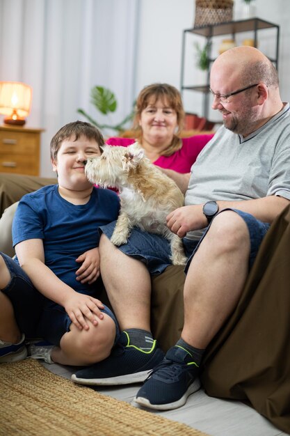 Foto un perro lamia la cara de un niño que está sentado en el sofá de la sala de estar con sus padres