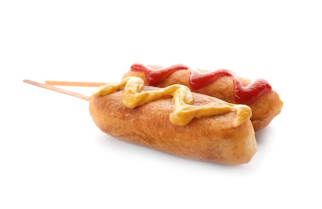 Perro de maíz sabroso con ketchup y mostaza sobre fondo blanco.