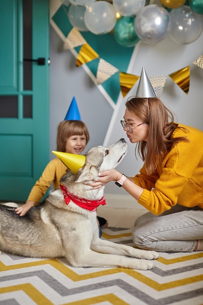 Perro mascota cumpleaños familia madre e hijo abrazan y besan a su perro felicitando feliz cumpleaños