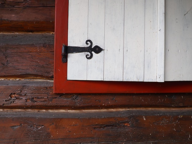 Persianas de madeira étnica em uma janela com moldura de madeira pintada de vermelho e branco Suporte de argola de metal em forma de flecha e coração Complexo arquitetônico Stanisici Bielina Bósnia Cabana de toras