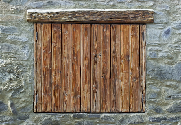 Persianas de madera cerradas sobre una fachada de piedra de un chalet de montaña.