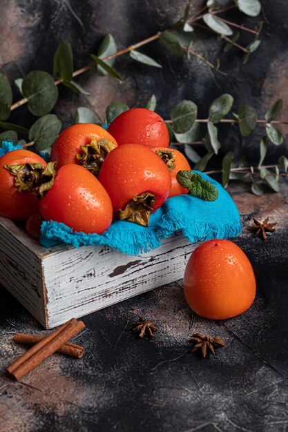Persimmon auf dunklem Hintergrund Frische reife Früchte auf einem blauen Teller und in einer Schachtel Gesundes Essen